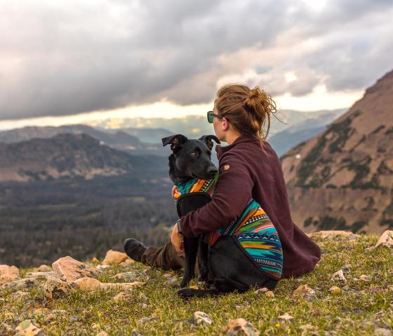 Girl and her dog sitting on the groud overlooking mountain landscape