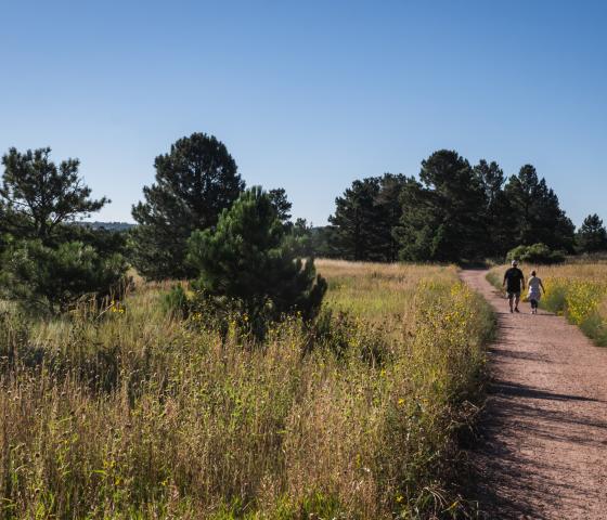 two people walk side my side on a wide gravel trail on a sunny day.