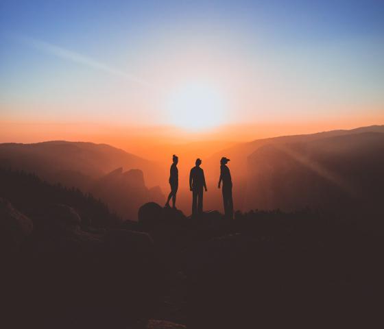 Three silhouettes stand infront of a canyon at sunrise. 