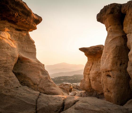 Sandstone formations frame hazy mountains at sunset.