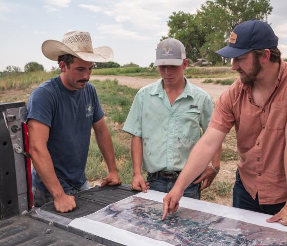 Three people review a map on the tailgate of a farm truck.